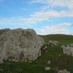 A large chert rock outrcopping on a green grassy hill with blue skies and clouds in the background.