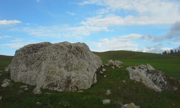 A large chert rock outrcopping on a green grassy hill with blue skies and clouds in the background.