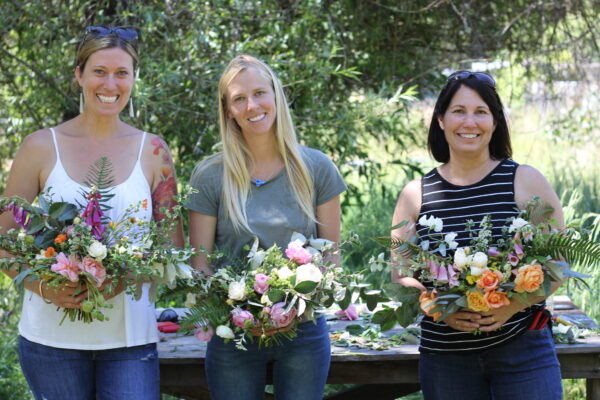 Three people smiling at the camera while holding bouquets at B Side Farm.