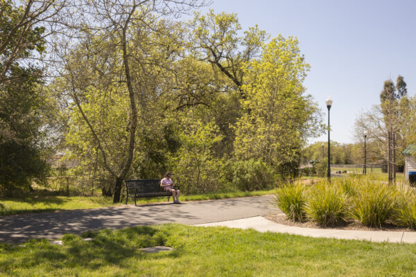 Person sitting on a bench, along a trail, with trees in the background, in Keiser Park.