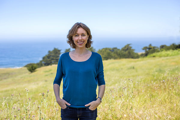 Supervisor Lynda Hopkins standing in a golden field with the ocean and a row of low, green trees in the background.